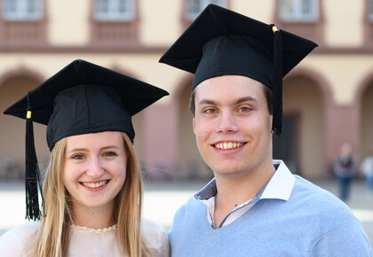 Eine Bachelorabsolventin und ein Bachelorabsolvent stehen vor dem Mannheimer Schloss.