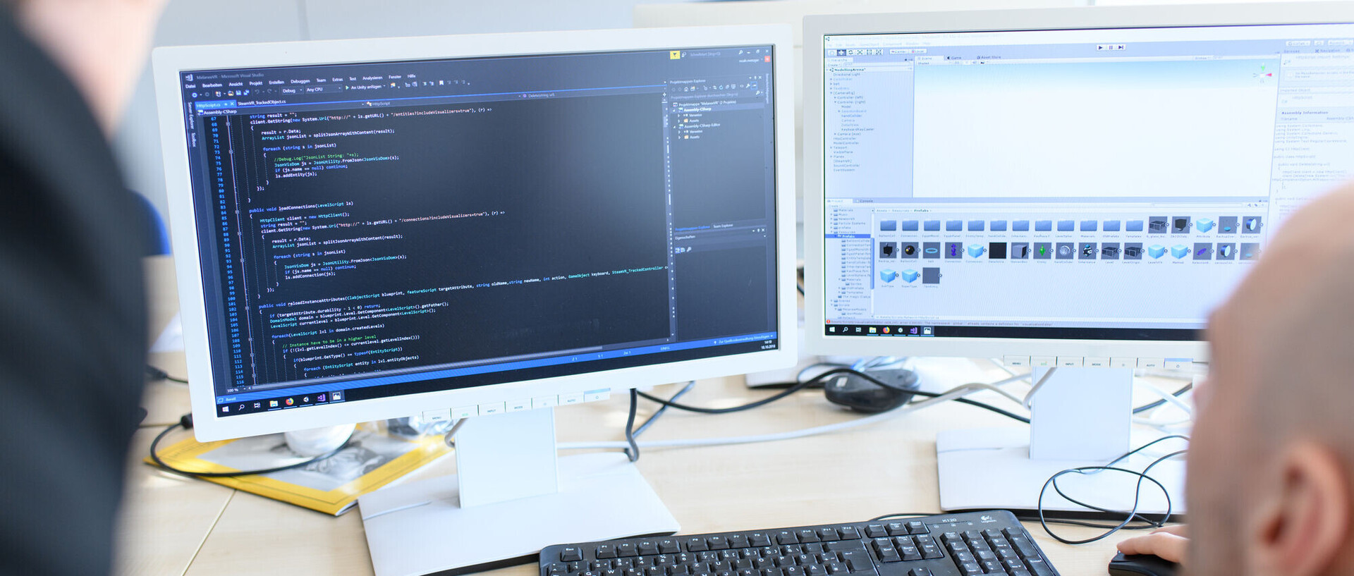 Zwei Forschende schauen auf zwei Monitore, auf denen Codes zu sehen sind. 