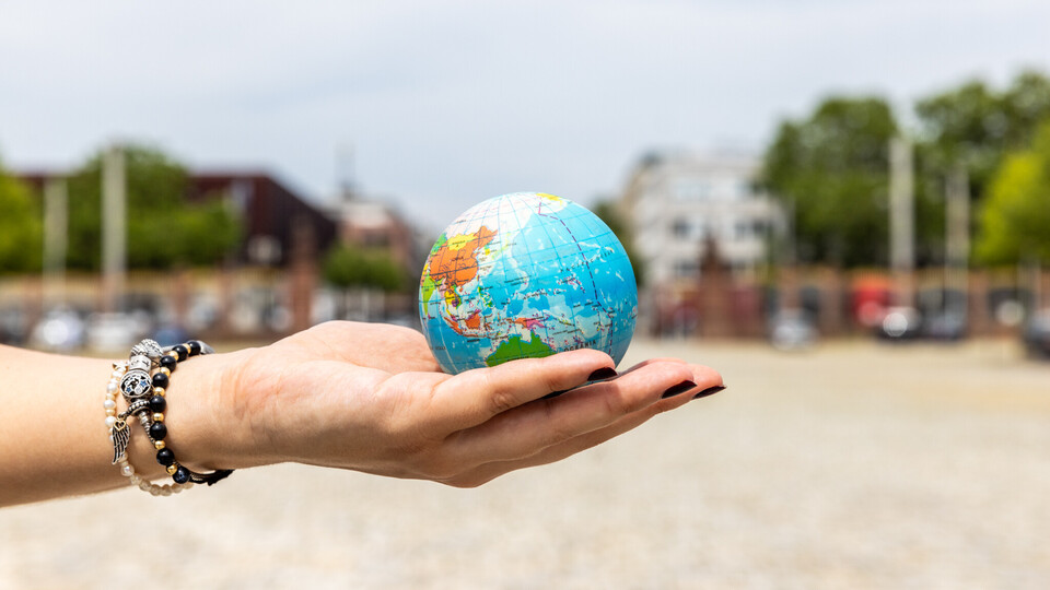 Student holding a globe in the palm of her hand. She is wearing three bracelets in black and silver and has black nail polish. 