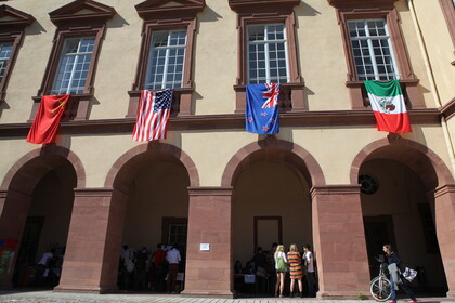 Innenhof mit Arkaden des Schlosses Mannheim, internationale Flaggen hängen über Gruppen von Menschen.