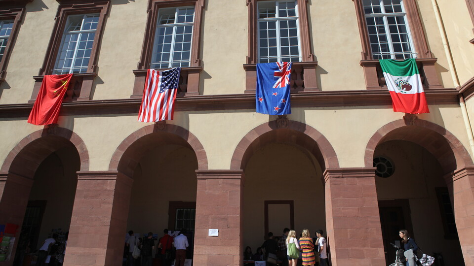 Innenhof mit Arkaden des Schlosses Mannheim, internationale Flaggen hängen über Gruppen von Menschen.