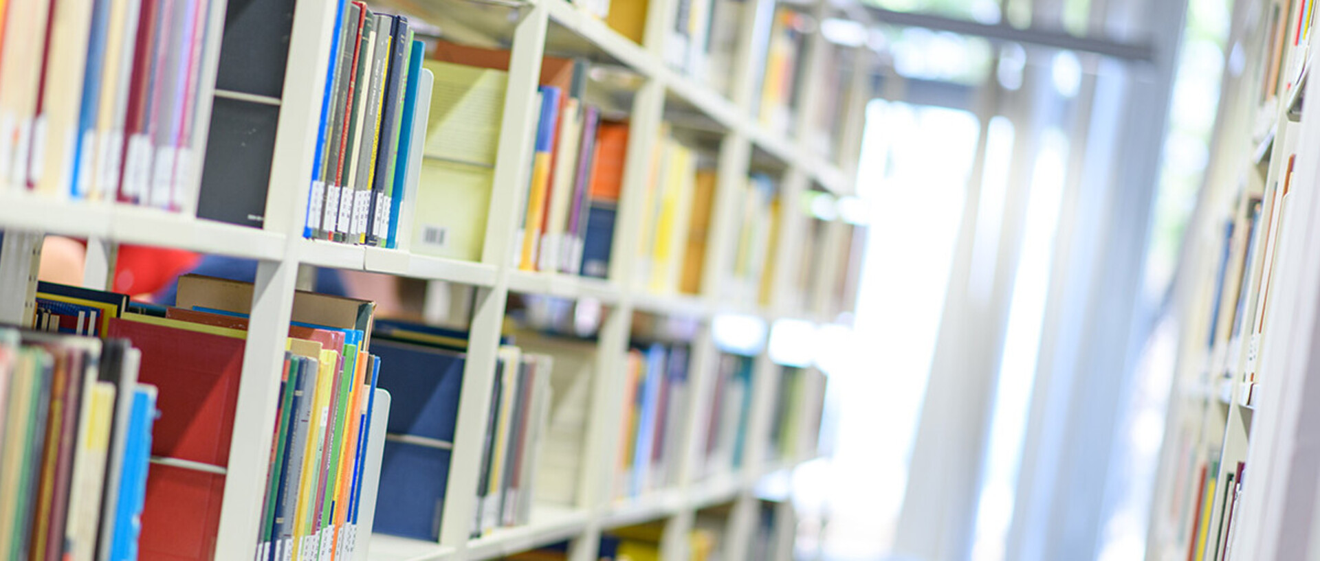 Helle Bibliothekregale mit vielen bunten Büchern.