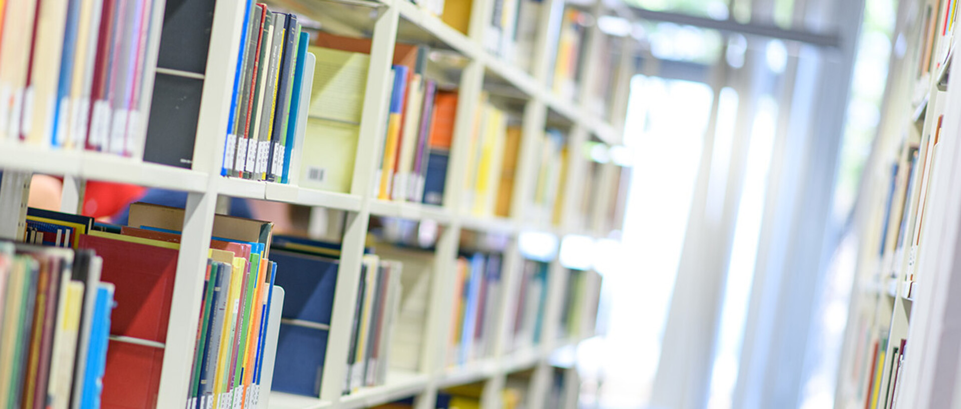 Helle Bibliothekregale mit vielen bunten Büchern.