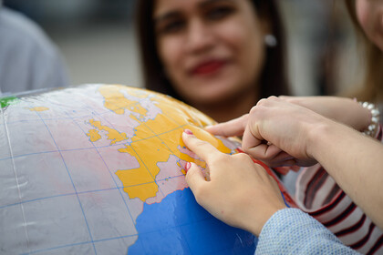 Drei Hände deuten auf einen Punkt auf einem Globus