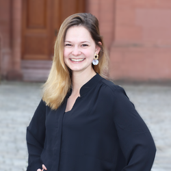 Jovita Lukasik. Sie hat blonde lange Haare und trägt eine schwarze Bluse und steht vorm Mannheimer Schloss
