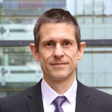 Martin Schlather hat kurze braune Haare. Er trägt einen schwarzen Anzug und eine lilane Krawatte.