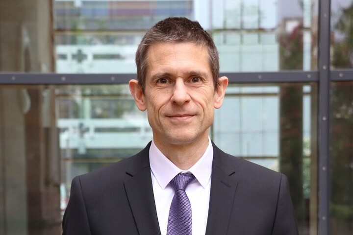 Martin Schlather hat kurze braune Haare. Er trägt einen schwarzen Anzug und eine lilane Krawatte.